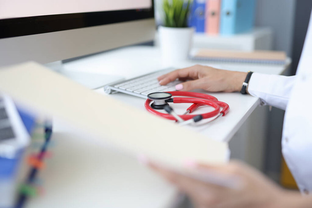 Op de werktafel in het medisch kantoor, de artsen hand op toetsenbord is naast stethoscoop - Foto, afbeelding