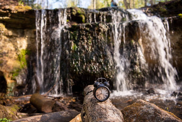 Retro alarm clock on waterfall background. Abstract photo of time. - Photo, Image