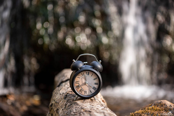 Retro alarm clock on waterfall background. Abstract photo of time. - Photo, Image