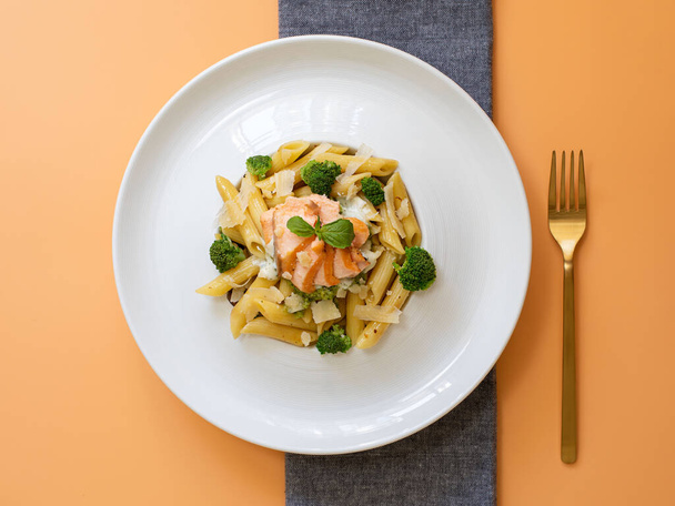 Pasta penne with salmon, broccoli, and pesto sauce on an orange background. Flat lay. - Foto, Imagen