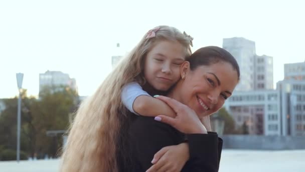 Detailní portrét mladé rodiny, roztomilé dcerušky objímají usmívající se matku s rukama za krkem od zad, koncept milujícího vztahu. Starší sestra drží dívku v náručí, podporuje uklidňuje dítě - Záběry, video