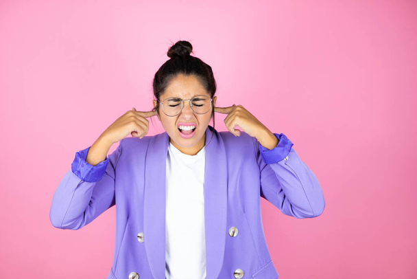 Young beautiful business woman over isolated pink background covering ears with fingers with annoyed expression for the noise of loud music. Deaf concept. - Photo, Image