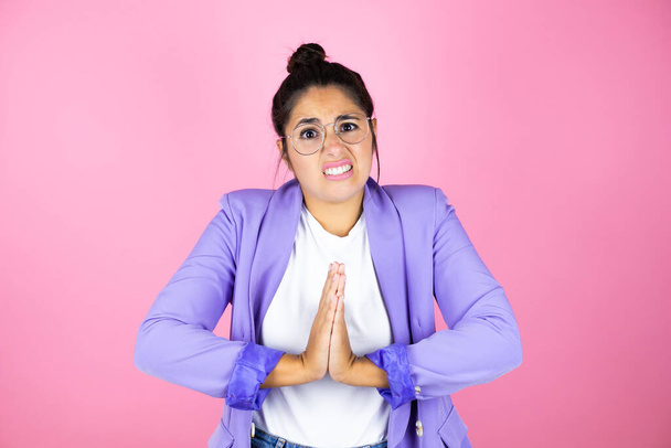 Young beautiful business woman over isolated pink background begging and praying with hands together with hope expression on face very emotional and worried - Photo, Image