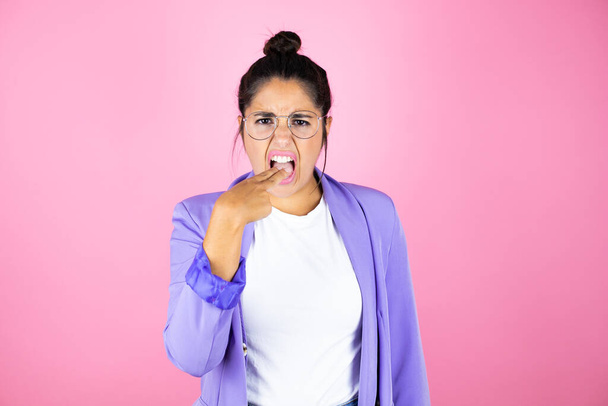Jovem bela mulher de negócios sobre isolado fundo rosa enojado com a mão dentro de sua boca - Foto, Imagem
