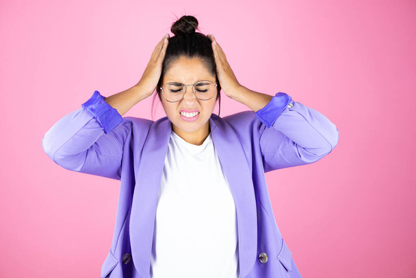 Молодая красивая деловая женщина на изолированном розовом фоне страдает от головной боли отчаяния и стресса, потому что боль и мигрень с руками на голове - Фото, изображение