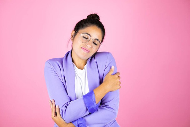 Junge schöne Geschäftsfrau vor isoliertem rosa Hintergrund, die sich glücklich und positiv umarmt, selbstbewusst lächelnd - Foto, Bild