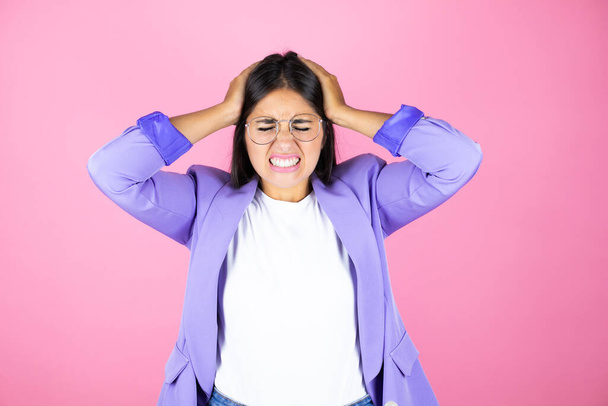 Jonge mooie zakenvrouw over geïsoleerde roze achtergrond lijdt aan hoofdpijn wanhopig en gestrest omdat pijn en migraine met haar handen op het hoofd - Foto, afbeelding