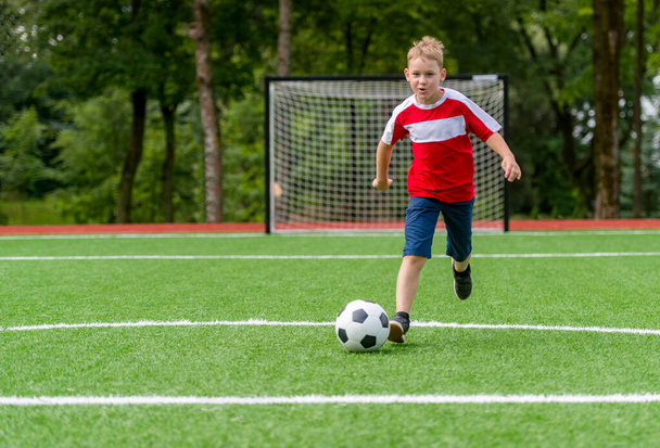 Jalkapallokoulutusta lapsille. Poika juoksee ja potkii jalkapalloa. Nuori poika parantaa jalkapallo taitoja - Valokuva, kuva
