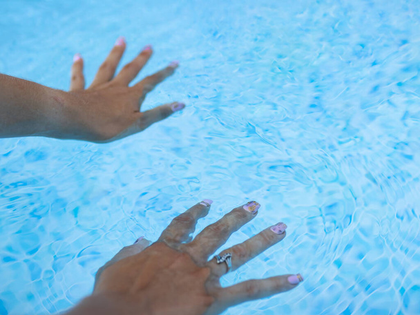 A jovem molha os dedos com unhas de gel na piscina. - Foto, Imagem