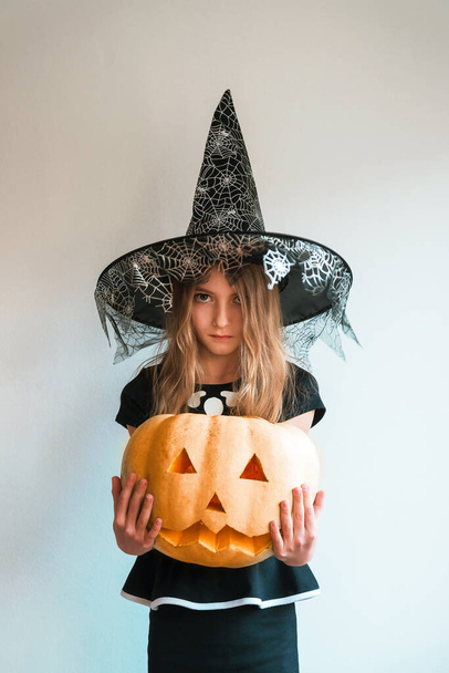 Young witch holds a Jack O Lantern pumpkin. Halloween concept. - Фото, изображение