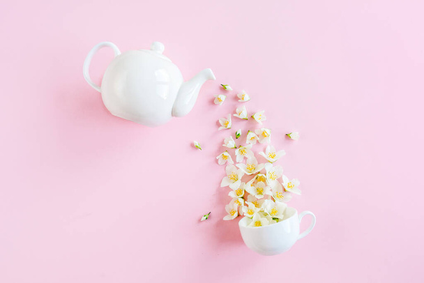 Creative layout of teapot and tea Cup with Jasmine flowers on a pink background. Jasmine tea. - Foto, imagen