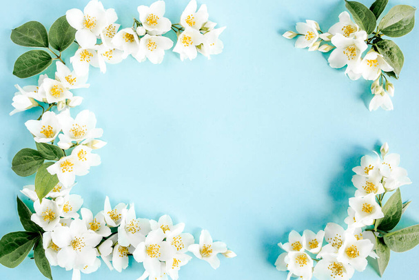 Frame of jasmine flowers, petals, leaves on blue background. Flat lay, top view  - 写真・画像