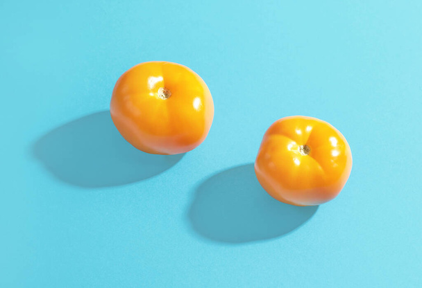 two yellow tomatoes with long shadows on blue paper background - Fotó, kép