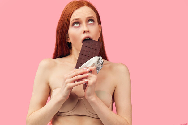 Young skinny anorexic woman holding chocolate bar, posing isolated on pink. - Zdjęcie, obraz