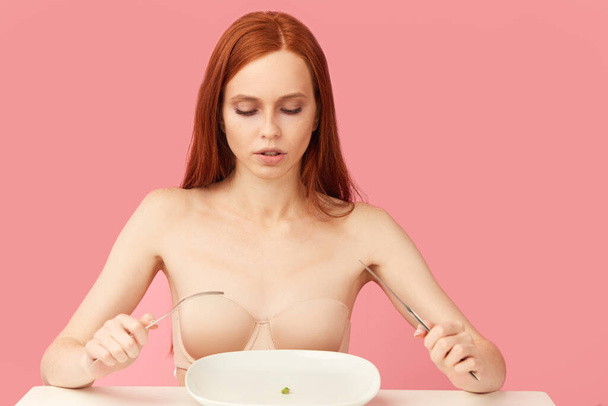 Red-haired woman looking at single green pea on white plate - Foto, immagini
