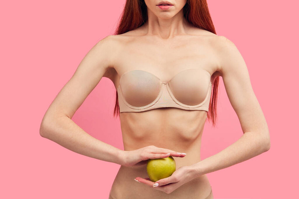Skinny woman with protruding ribs holding green apple isolated on pink, macro - Foto, afbeelding