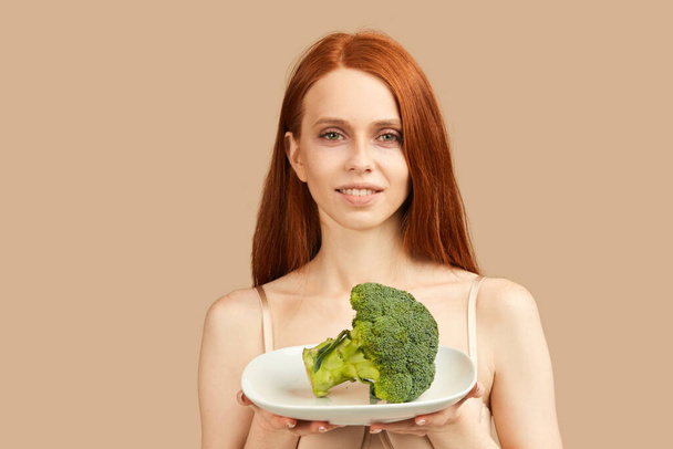 Skinny woman in underwear holding broccoli, licking, wants to eat it very much - Photo, image