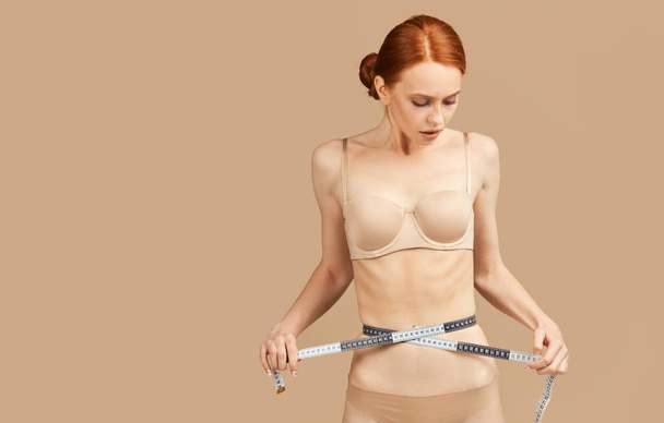 Caucasian model in underwear proud of diet results, measuring waist with tape - Foto, Imagen