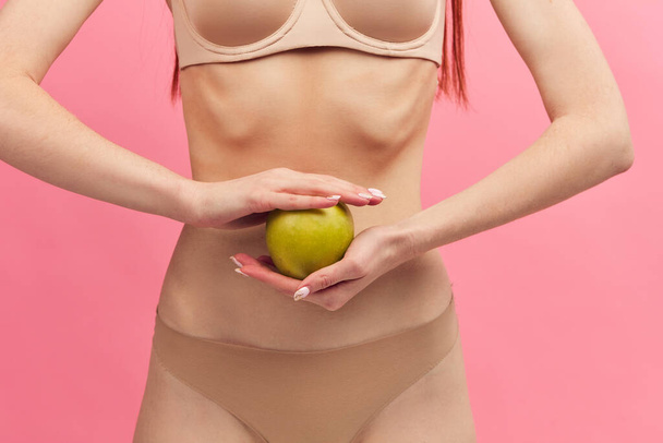 Skinny woman with protruding ribs holding green apple isolated on pink, macro - Fotografie, Obrázek