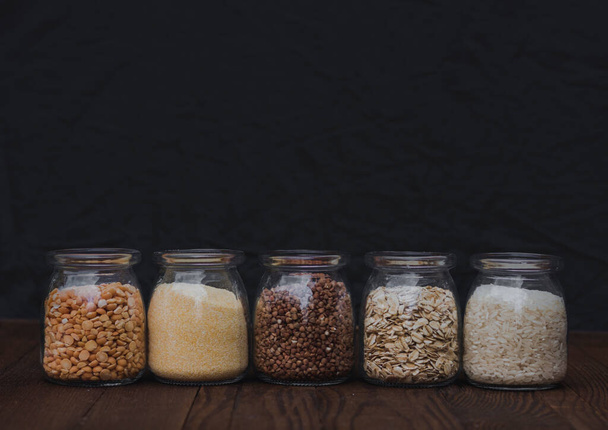 Pięć różnych rodzajów zbóż w słoikach na czarnym tle. Owsianka. Zdrowa żywność - Zdjęcie, obraz