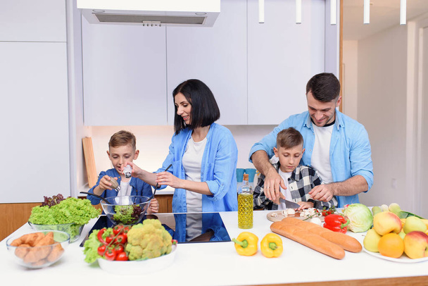 Happy caucasian family with two sons preparing healthy vegetarian breakfast with and vegetables on cozy kitchen. - 写真・画像