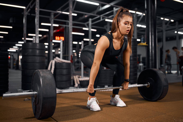 Young fit woman lifting barbell in fitness center - Photo, Image