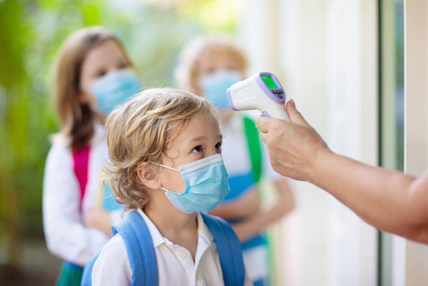 Temperature screening and medical check at school. Child in face mask in class in covid-19 outbreak. Teacher with thermometer at preschool entrance. Social distancing. Coronavirus prevention. - Photo, Image