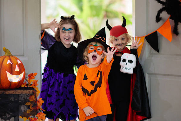 Kids trick or treat on Halloween night. Child at decorated house door. Boy and girl in witch and vampire costume and hat with candy bucket and pumpkin lantern. Autumn decoration. Friends play. - Photo, Image