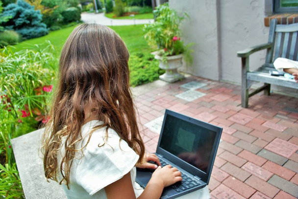 νεαρή κοπέλα που κάνει σχολικές εργασίες σε ένα υπολογιστή εξ αποστάσεως μάθηση στο πάρκο - Φωτογραφία, εικόνα