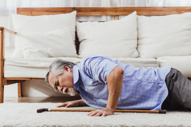 Asian senior man falling down lying on floor at home alone. Elderly man pain and hurt from osteoporosis sickness or heart attack. Old adult life insurance with health care and treatment concept - Valokuva, kuva