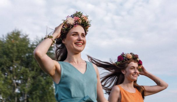 Two young and lovely girls in flower wreaths in nature. Ancient pagan origin celebration concept. Summer solstice day. Mid summer. - Φωτογραφία, εικόνα
