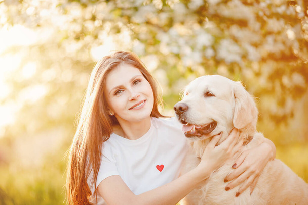 Beautiful girl hugs Labrador Retriever dog in summer park, sunset sunlight. Animals best friends concept - Photo, Image