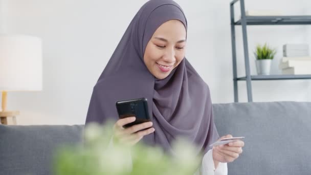 Asia muslim lady use smart phone, credit card buy and purchase e-commerce internet in living room at house. Stay at home, online shopping, self isolation, social distance, quarantine for coronavirus. - Materiaali, video