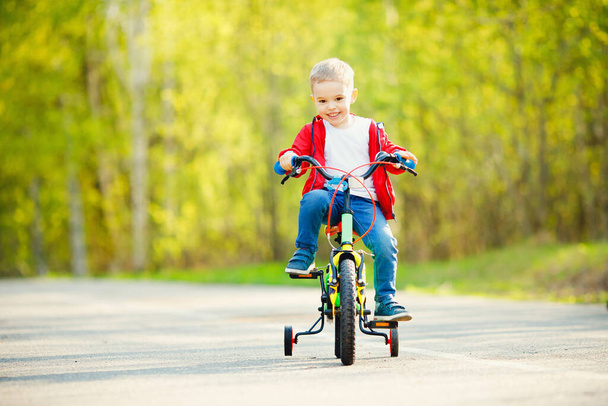 Happy boy rides bicycle and smiles in summer park. Ride training concept - Фото, зображення