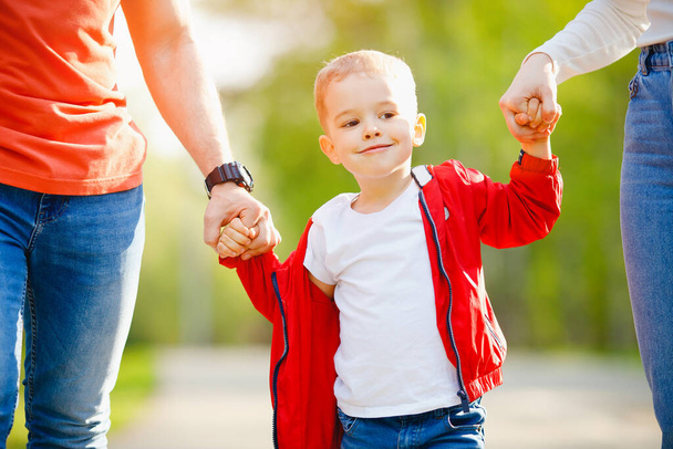 Happy baby boy sostiene a los padres de las manos en el parque, retrato de cerca. Concepto de paseo familiar - Foto, Imagen