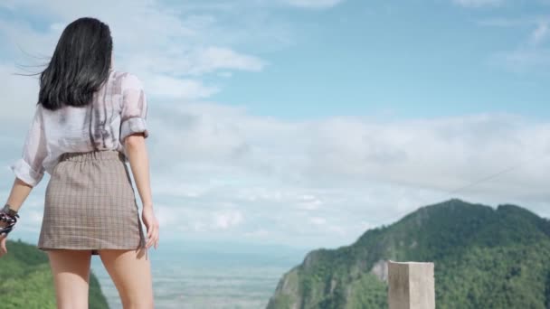 Mladá asijská žena pocit svěží tím, že stojí na vrcholu hory natáhnout paže a silný vítr fouká, při pohledu na vesnici mraky nebe, krásné přírody, pocit čerstvého vzduchu, tropické cestování.  - Záběry, video