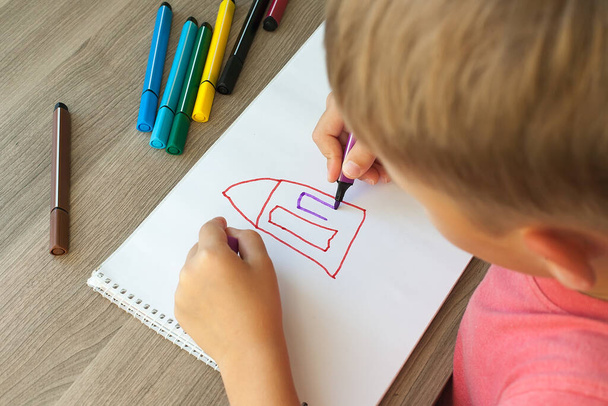 Ένα μικρό παιδί ζωγραφίζει ένα σπίτι με μαρκαδόρους στο άλμπουμ. Οδηγίες βήμα προς βήμα - Φωτογραφία, εικόνα