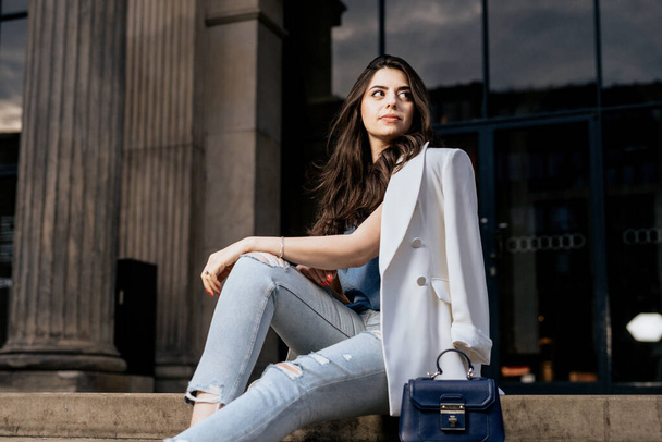 Attractive woman wearing white fashion jacket and jeans look away. Young woman on building background - Photo, Image