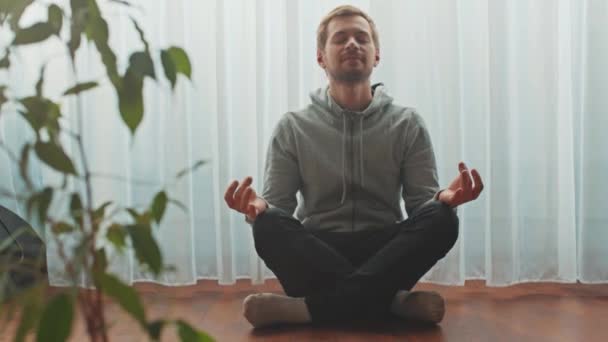 Young practices yoga and meditates in the lotus position at home.  - Footage, Video