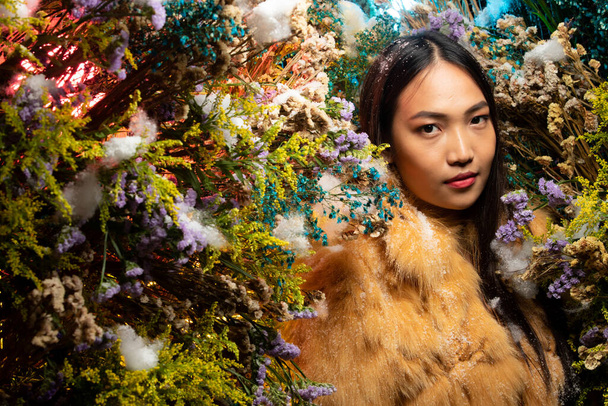Krásná romantická mladá asijská žena v Fox Fur látky v keři různých květin pózovat na pozadí čerstvé a sušené flóry. Inspirace podzimního zimního sněhu Parfém, kosmetický koncept. - Fotografie, Obrázek