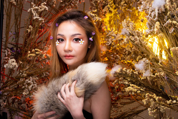 Beautiful romantic young Asian woman in Fox tail in bush variety of flowers posing on background fresh and dried flora. Inspiration of autumn winter snow Perfume, cosmetics concept. - Photo, Image