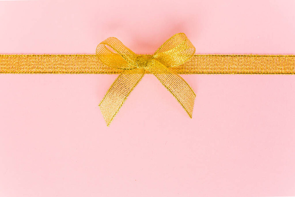 Gold ribbon with bow, isolated on pink background. Colorful celebration, birthday background. Flat lay, top view - Fotoğraf, Görsel