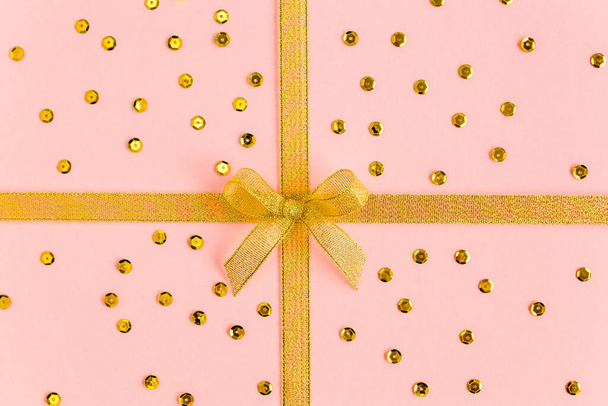 Gold ribbon with bow, isolated on pink background. Colorful celebration, birthday background. Flat lay, top view - 写真・画像