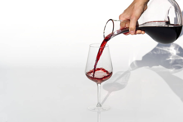 Sommelier giet rode wijn van decanter tot wijnglas op witte achtergrond. - Foto, afbeelding