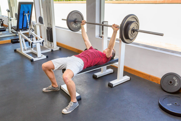 Young dutch man bench press with barbell in fitness room - Foto, afbeelding