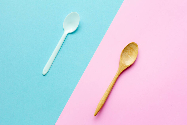 Flat lay wooden spoon with plastic spoon on pink and blue background.sustainable lifestyle and zero waste concept - Foto, imagen