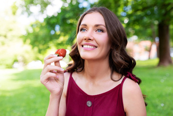 happy woman eating strawberry at summer park - Foto, Bild