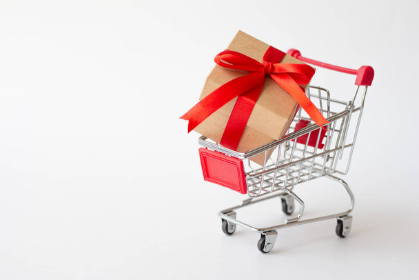 Gift box on miniature shopping cart on white background. - Fotografie, Obrázek