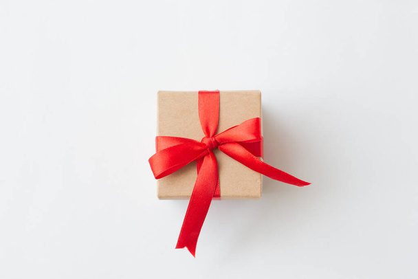 Brown paper gift box with red ribbon on white background. - Фото, изображение