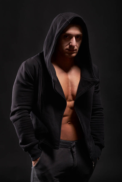Bodybuilder standing in black hoodie. Studio shot. Isolated - Foto, afbeelding